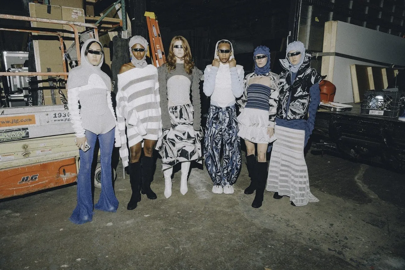 Six models in unique textured knitwear, sunglasses, and balaclavas posing backstage.