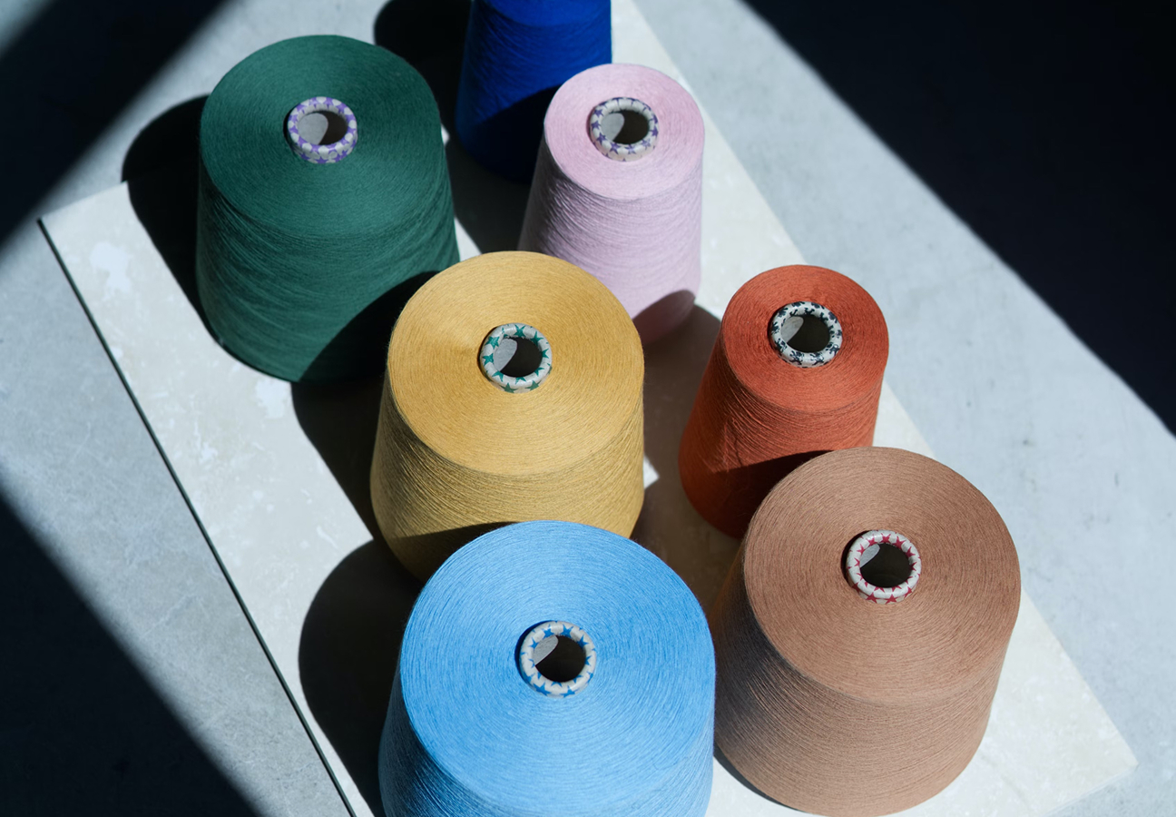 Various colored spools of yarn, including green, pink, yellow, orange, blue, and brown, arranged on a table.