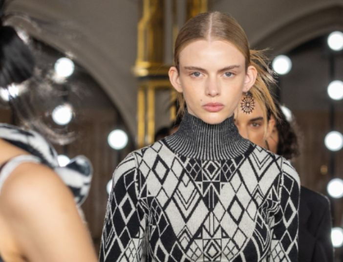 A model with pulled-back hair wears a black and white geometric patterned turtleneck sweater.